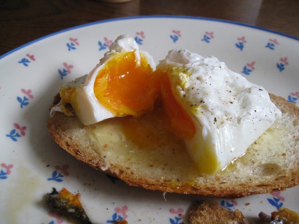 A poached egg cut open on buttered toast, with the yolk spilling onto the plate