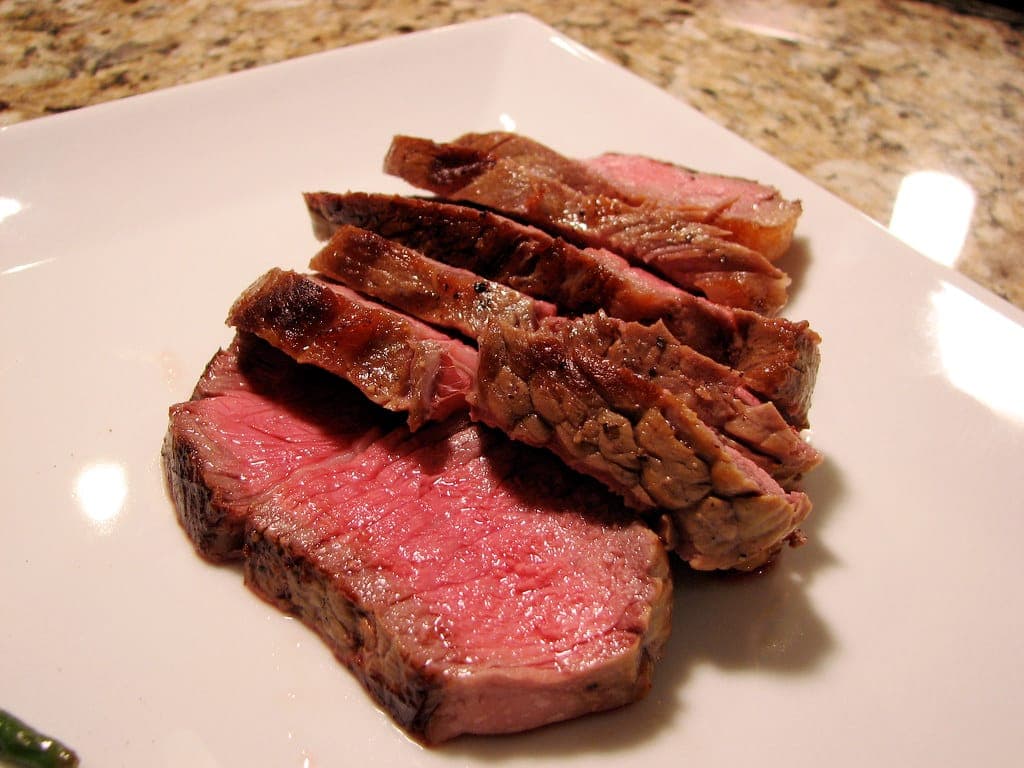 Slices of seared steak with a pink, medium-rare centre on a white plate