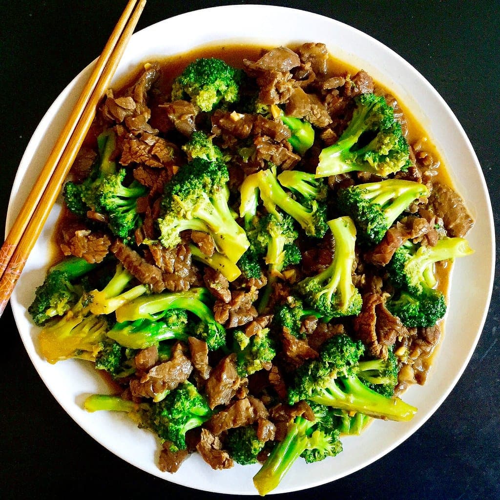 A white plate piled with glossy strips of stir-fried beef and broccoli florets, with chopsticks on the side