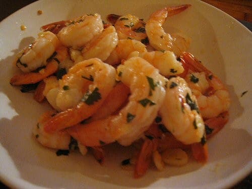 A plate of seared pink shrimp glistening with garlic butter and flecked with chopped parsley
