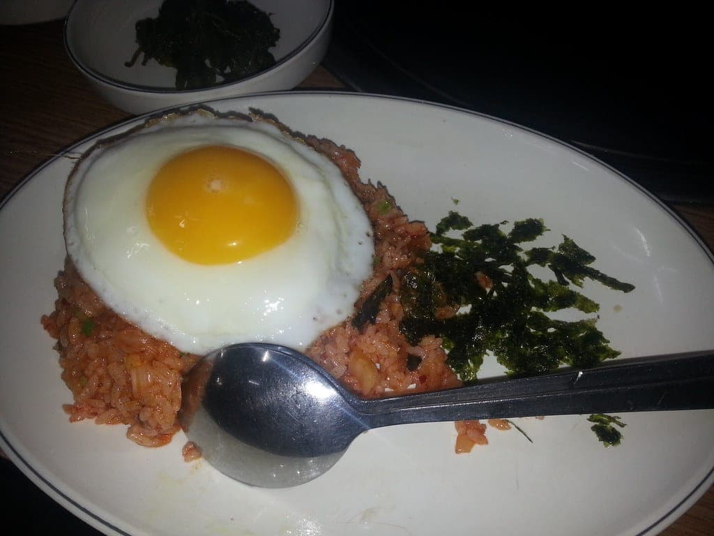 A plate of red kimchi fried rice topped with a sunny-side-up egg and strips of roasted seaweed