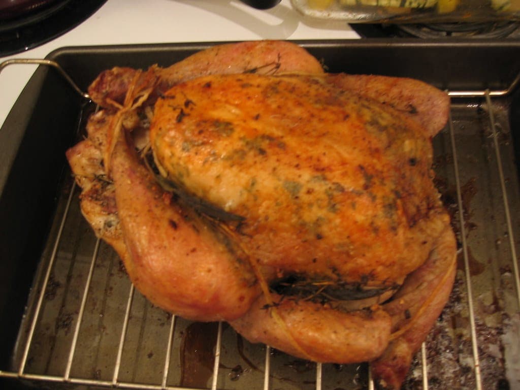 A golden roast chicken flecked with herbs, sitting on a wire rack in a roasting pan